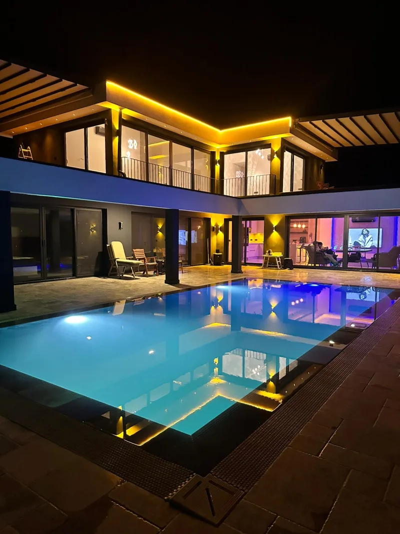Gece turkuaz ışıklı infinity havuz ve modern villa cephesi Göcek
