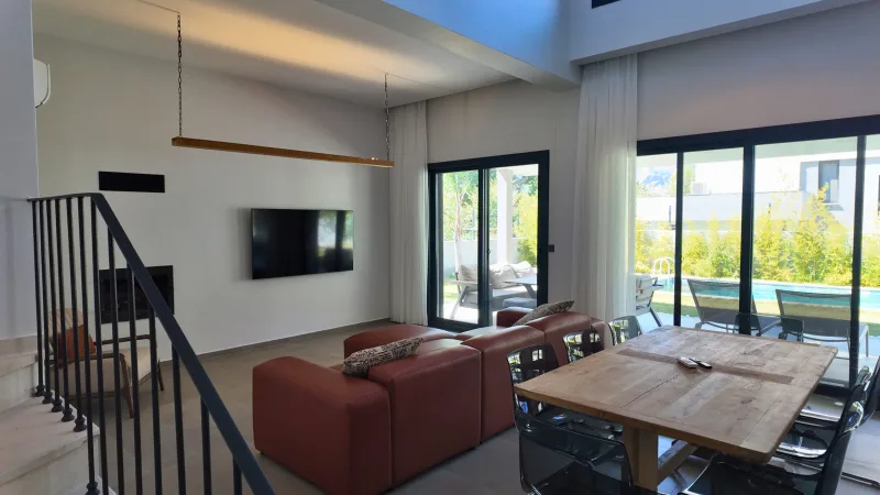Şömine ve terrakota koltuklu açık plan salon; cam kapılardan havuz ve bahçe manzarası, Göcek villa
