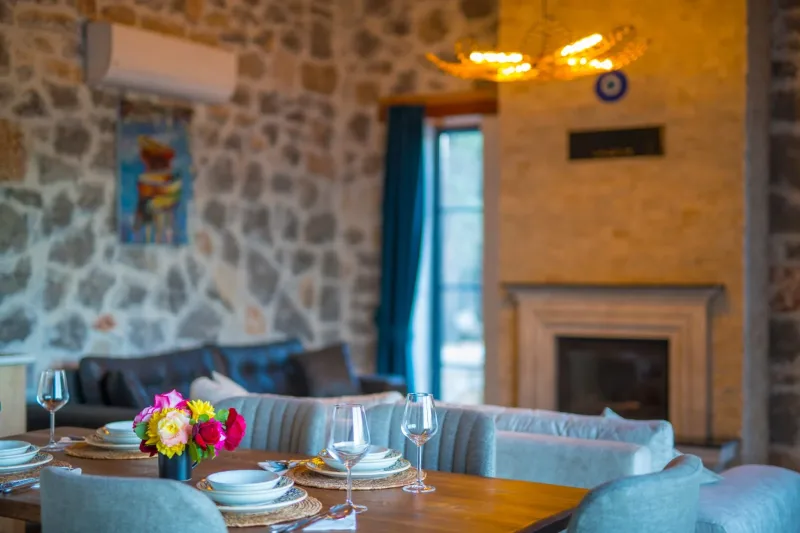 İnlice taş villa salon; şömineli doğal taş duvar, çiçekli ahşap yemek masası ve nazar boncuğu