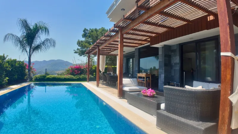Özel havuz kenarında ahşap pergolalı veranda, beyaz minderli rattan oturma grubu