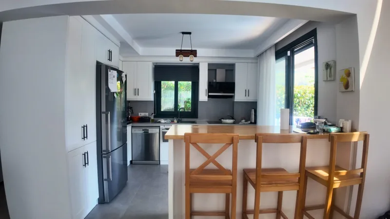 Beyaz dolaplı modern mutfak, paslanmaz buzdolabı, ocak davlumbazı ve ahşap ada tabureleri